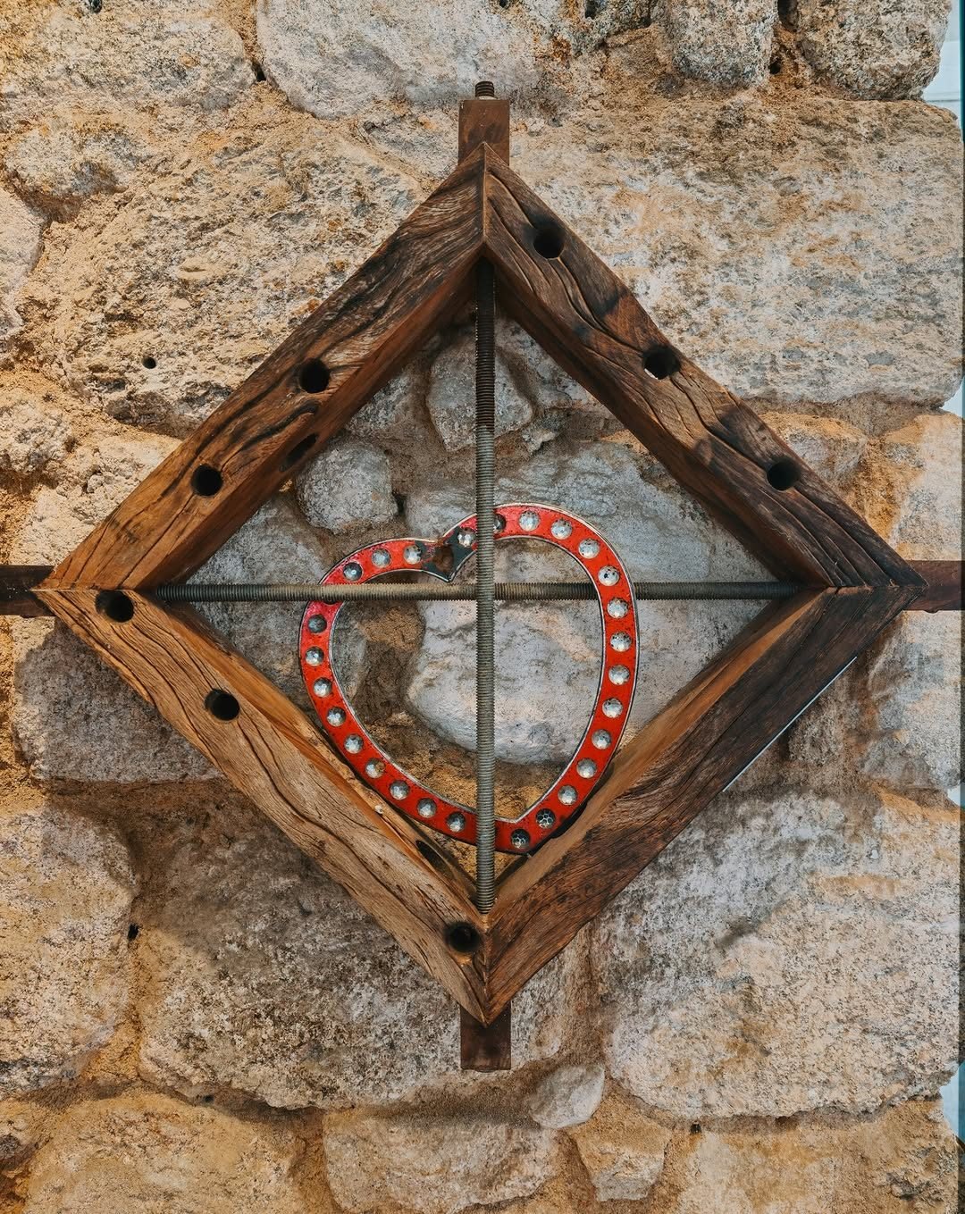 The work Auto Engano mounted on a stone wall with a diamond wood frame and a red heart.