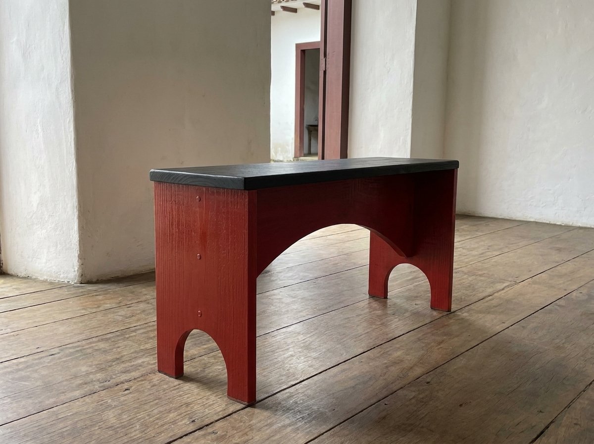 Banco Arco with an arched red wooden base and black seat on a wide plank floor before white walls.