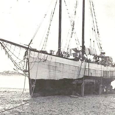 Wooden hull of a sailing boat supported on sand at low tide in black and white.