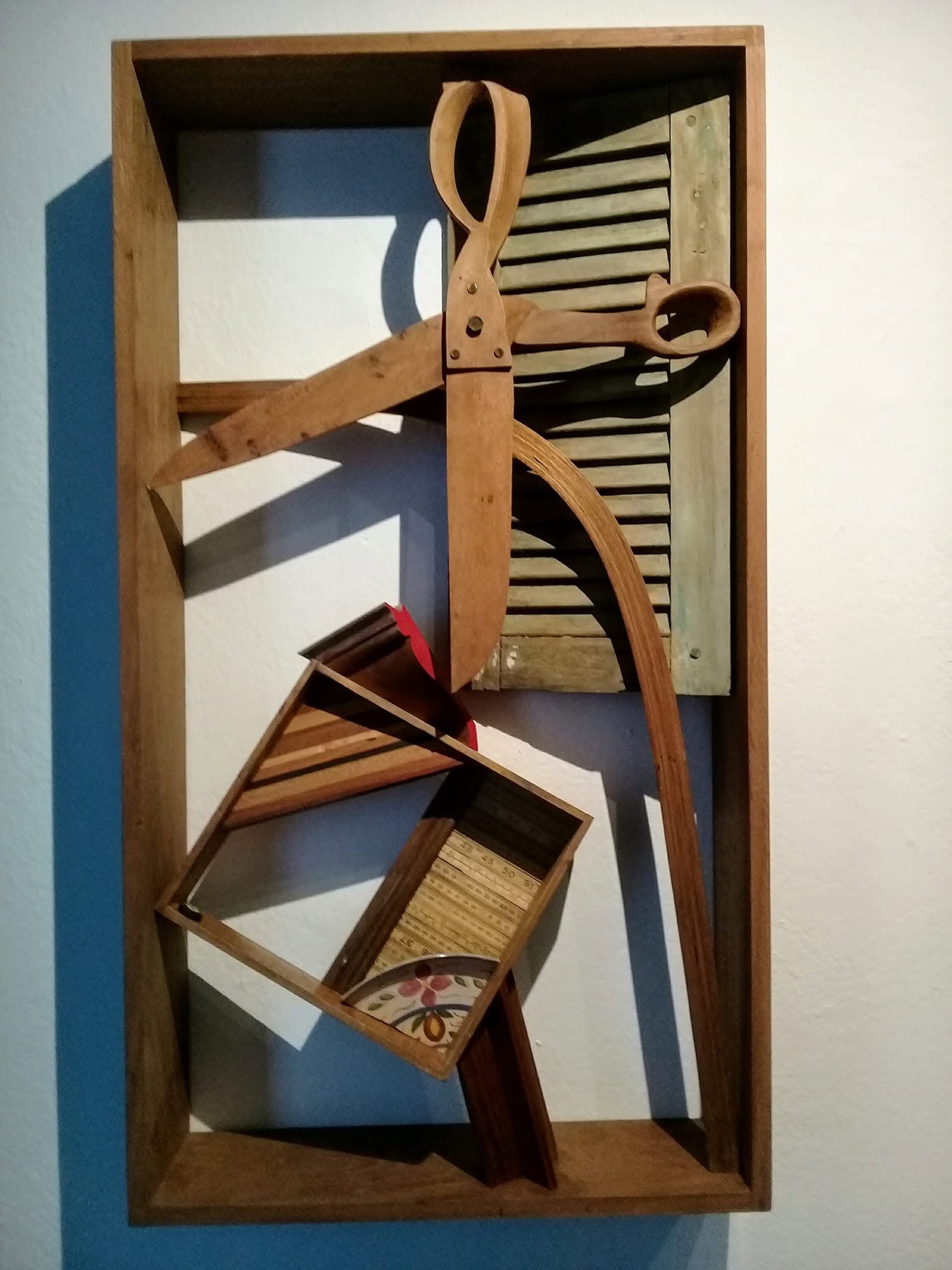 The wall work Caixa 04 features wooden forms, a large pair of wooden shears, and slats against a light wall.