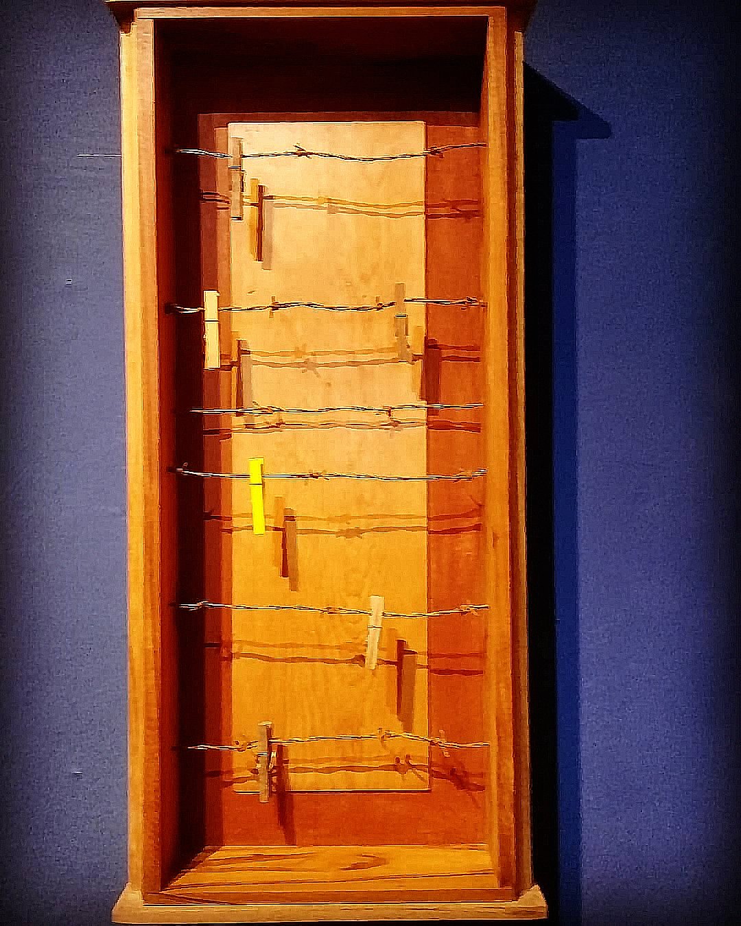 Caixa 09, a tall wooden wall box containing horizontal strands of wire with attached wooden pegs.