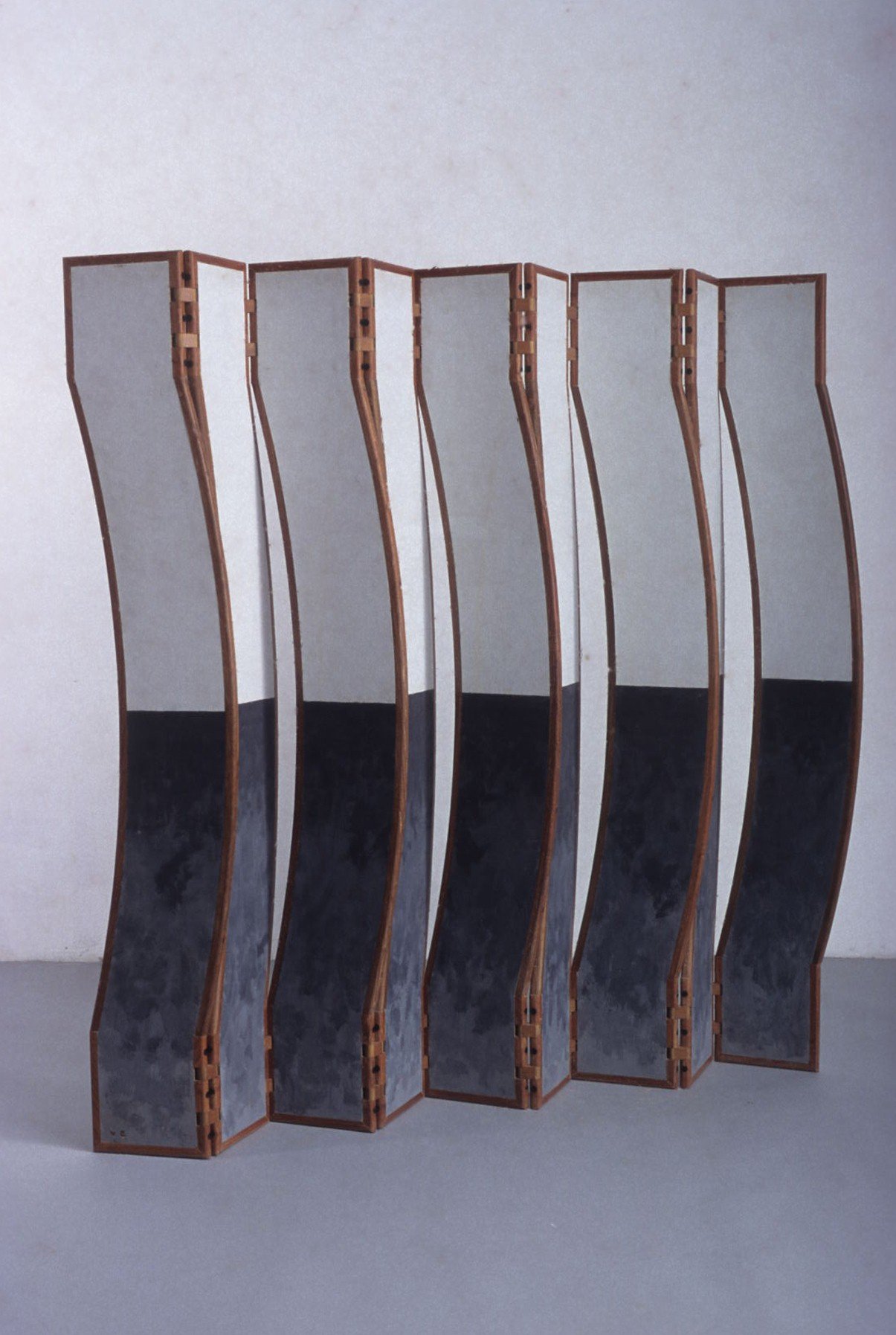 Mobile sculpture with sinuous vertical panels divided into white and black halves standing on a grey floor.