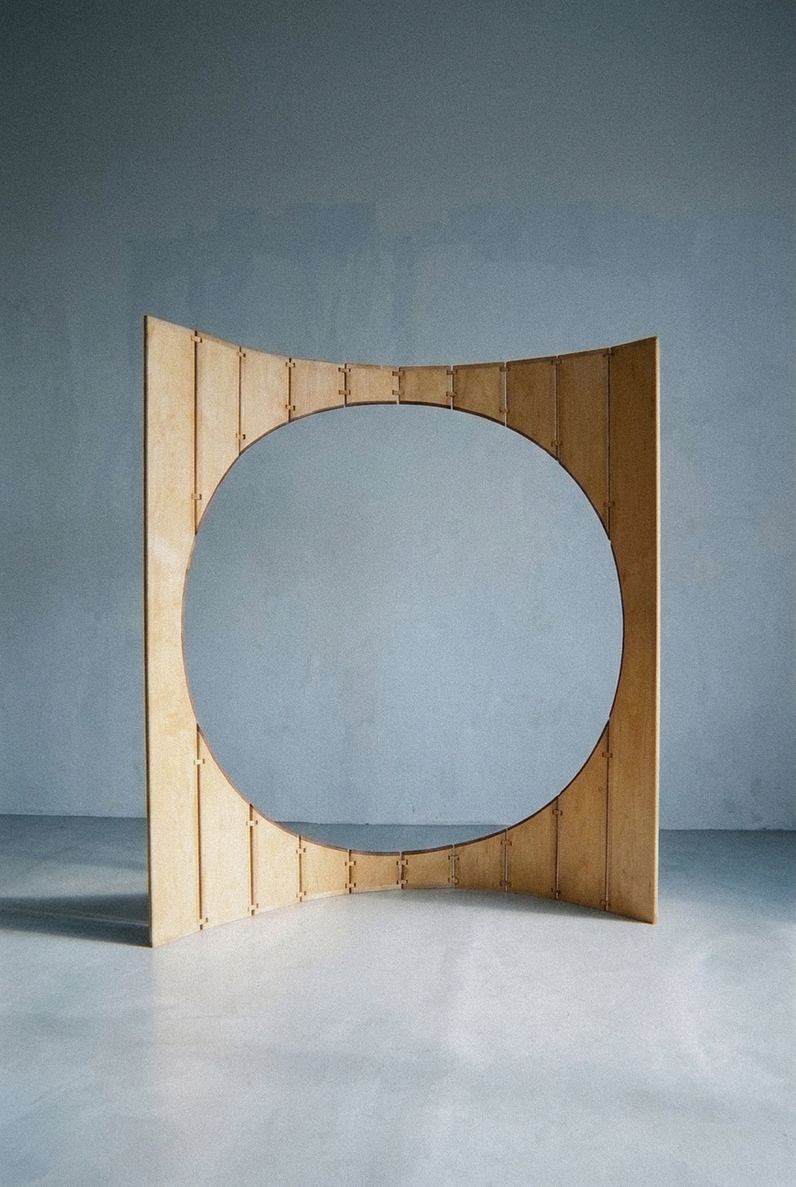 The mobile sculpture Ó in wood and brass stands in an open curve with a large circular cutout.
