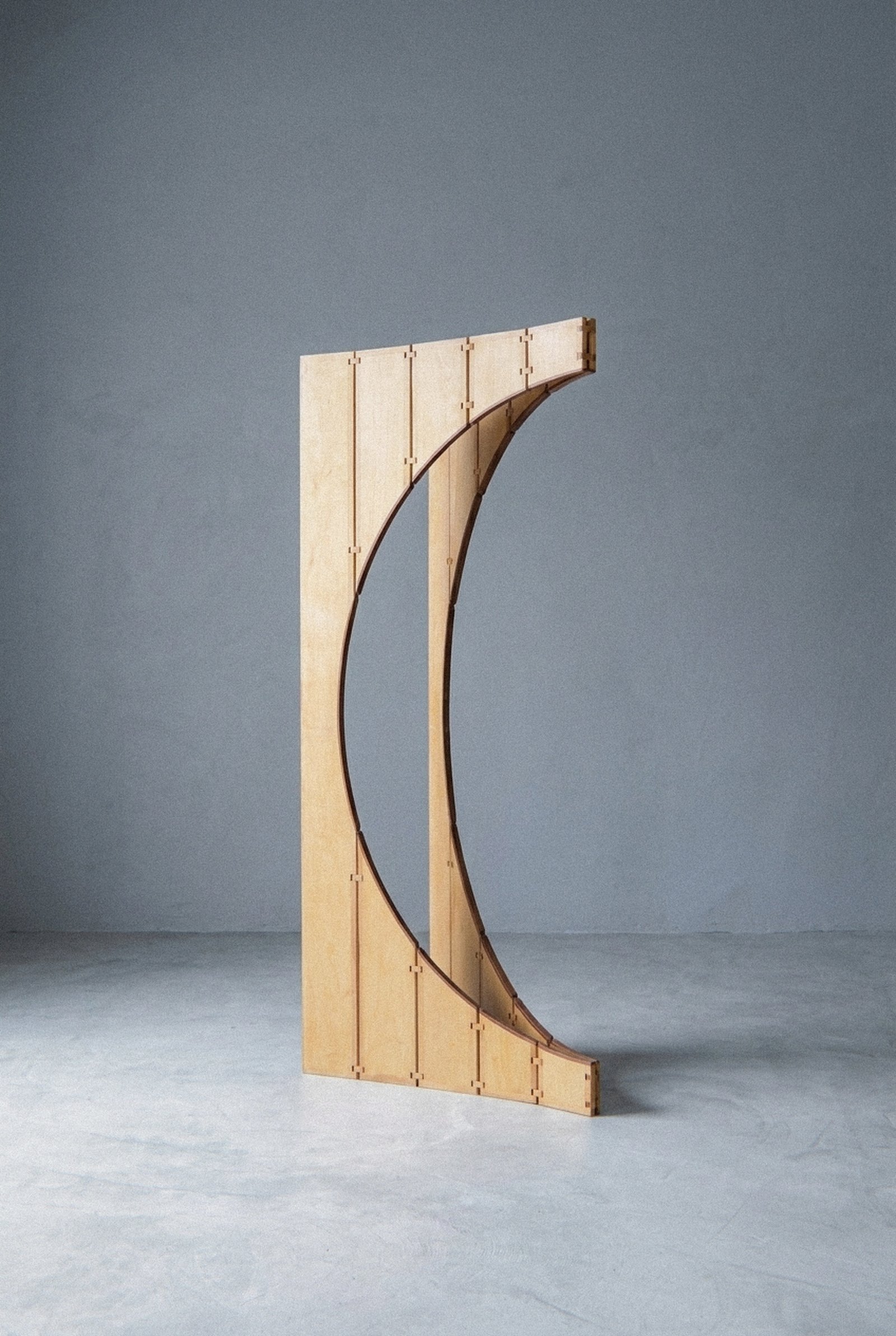 A escultura móvel Ó aberta em meia lua sobre piso de concreto diante de parede cinza clara.