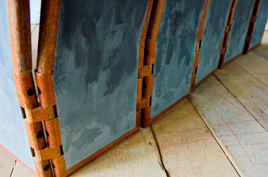 Lower detail of the mobile sculpture Fêmea showing wooden hinges with brass fittings and grey paint on the wood.