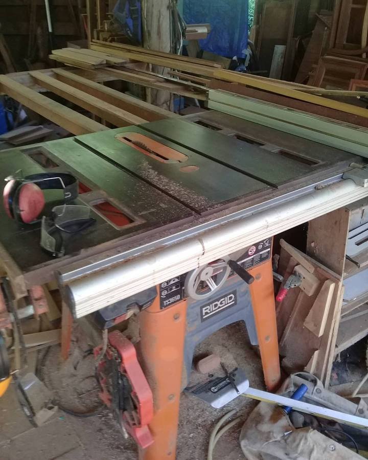 A table saw with wooden boards and ear defenders inside a workshop.