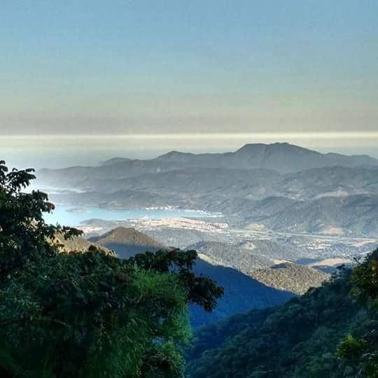 Wide view of forested mountains with the sea and coastline in the distance under clear sky.
