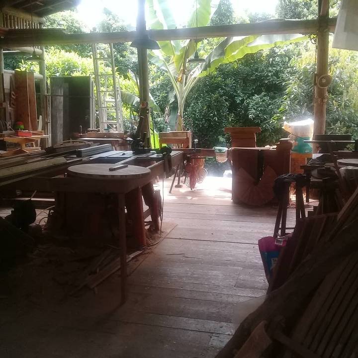 Open woodworking workshop floor with saws and benches looking out onto green foliage.