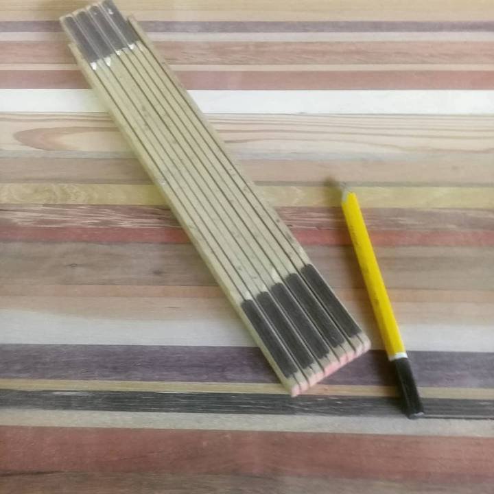 A folded wooden ruler and a yellow pencil rest on a surface of multicoloured wooden strips.