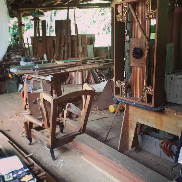The workshop interior with an unfinished wooden armchair frame, a vertical box sculpture, and timber planks.