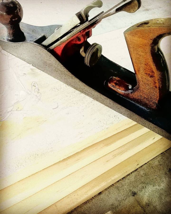 A metal and wood hand plane rests diagonally across light wooden strips.