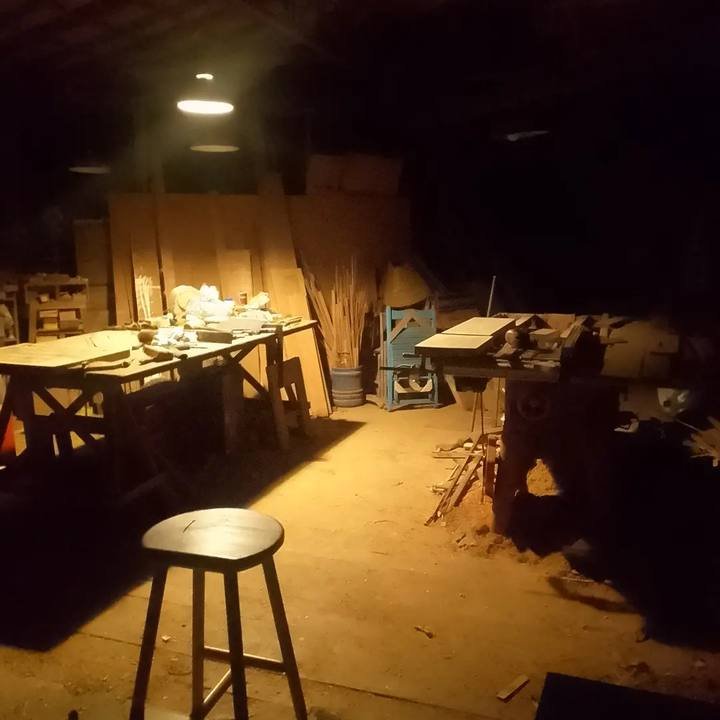The workshop at night under an overhead light showing a workbench, tools, machinery, and a stool.