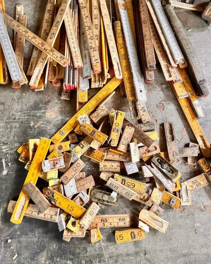 Cut fragments of yellow folding rulers and wooden measuring sticks scattered on a concrete floor.
