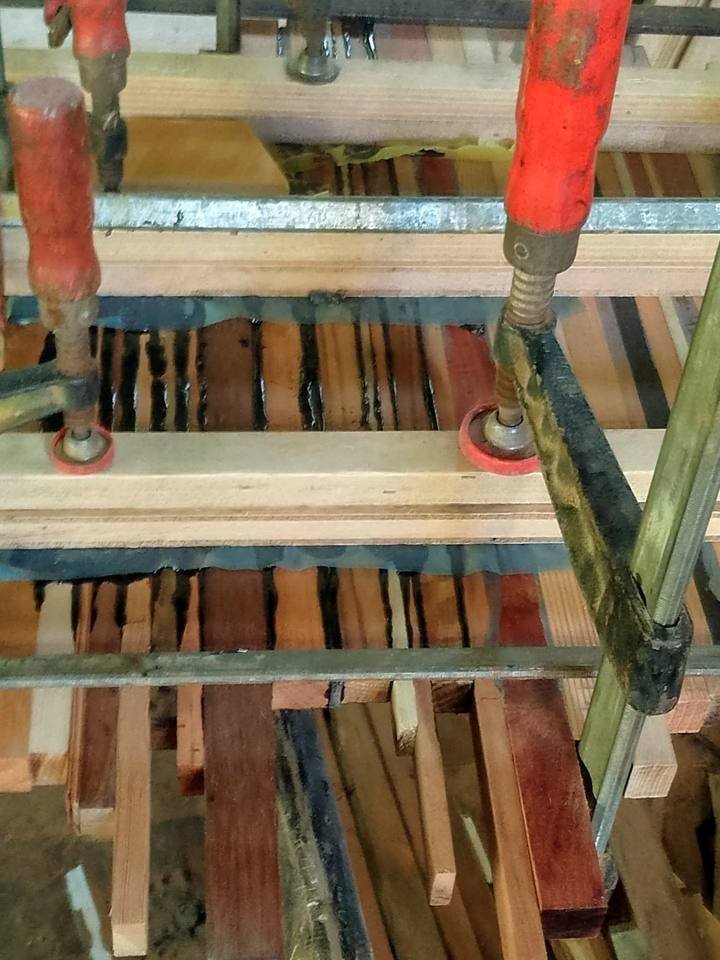 Close view of wooden slats glued together under pressure from several clamps.