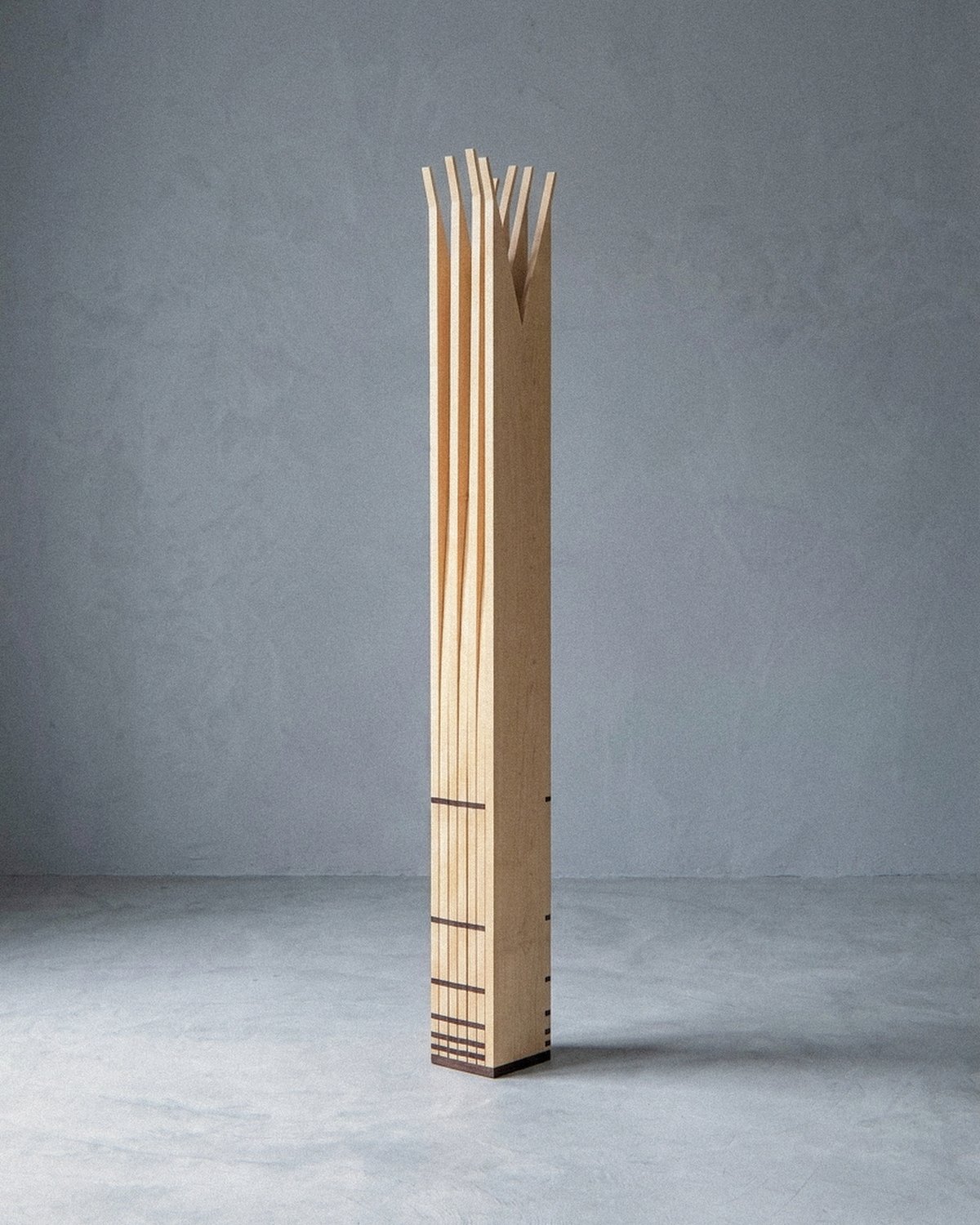 The mobile sculpture Velas standing complete at a distance, closed into a narrow vertical column on grey floor.