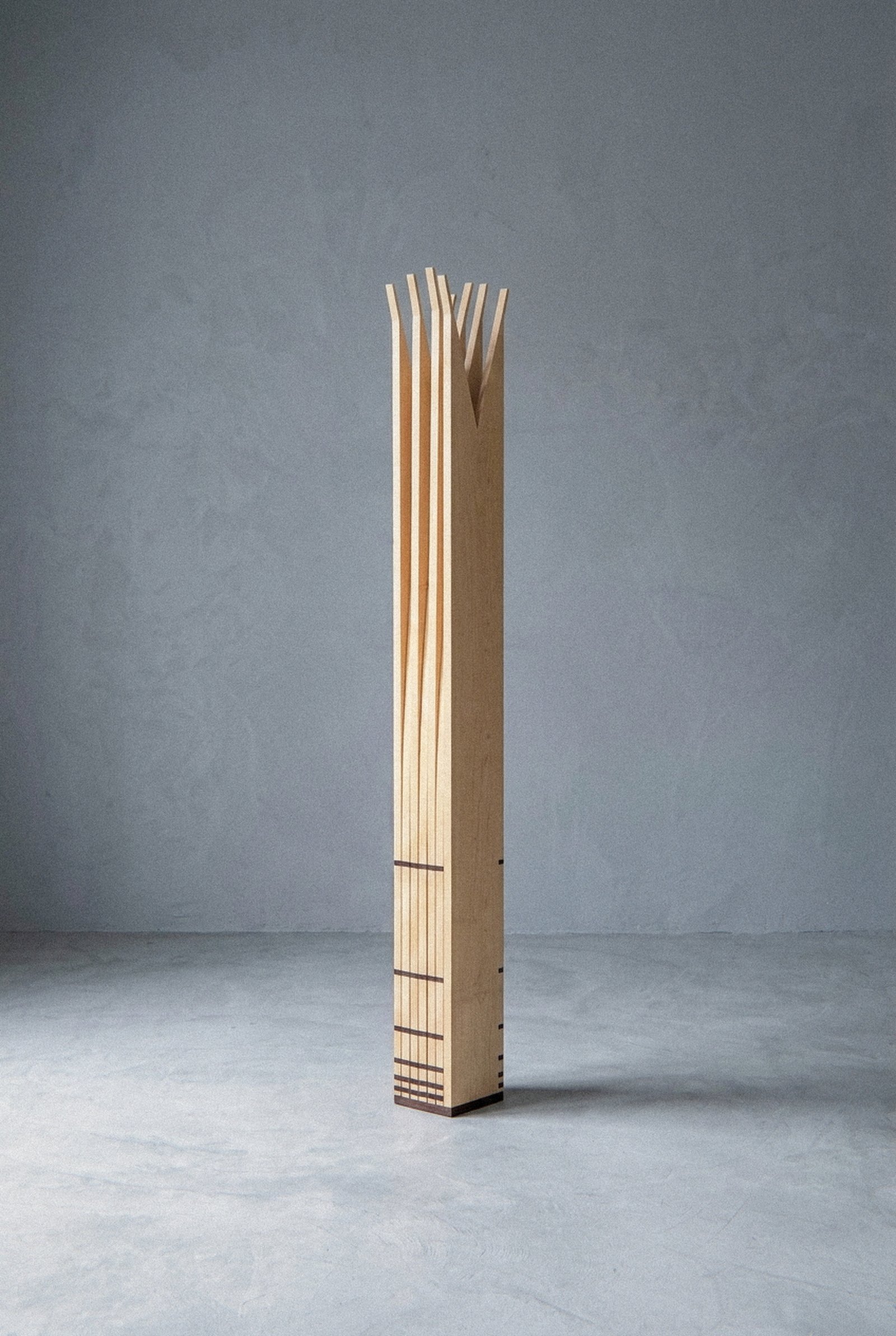 The mobile sculpture Velas standing complete at a distance, closed into a narrow vertical column on grey floor.