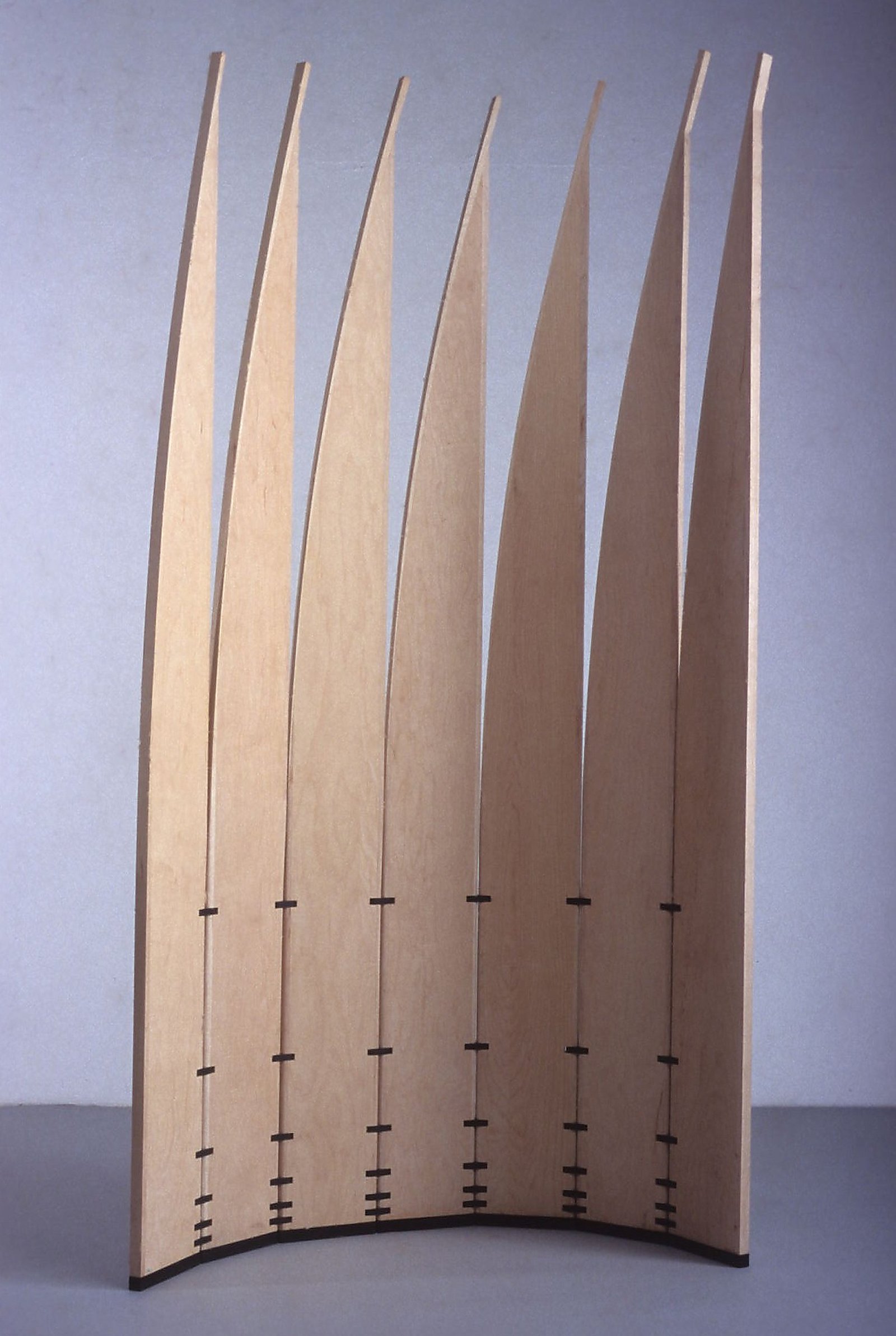 Photograph of the mobile sculpture Velas standing in an open curve against a light background, showing all pale blades.