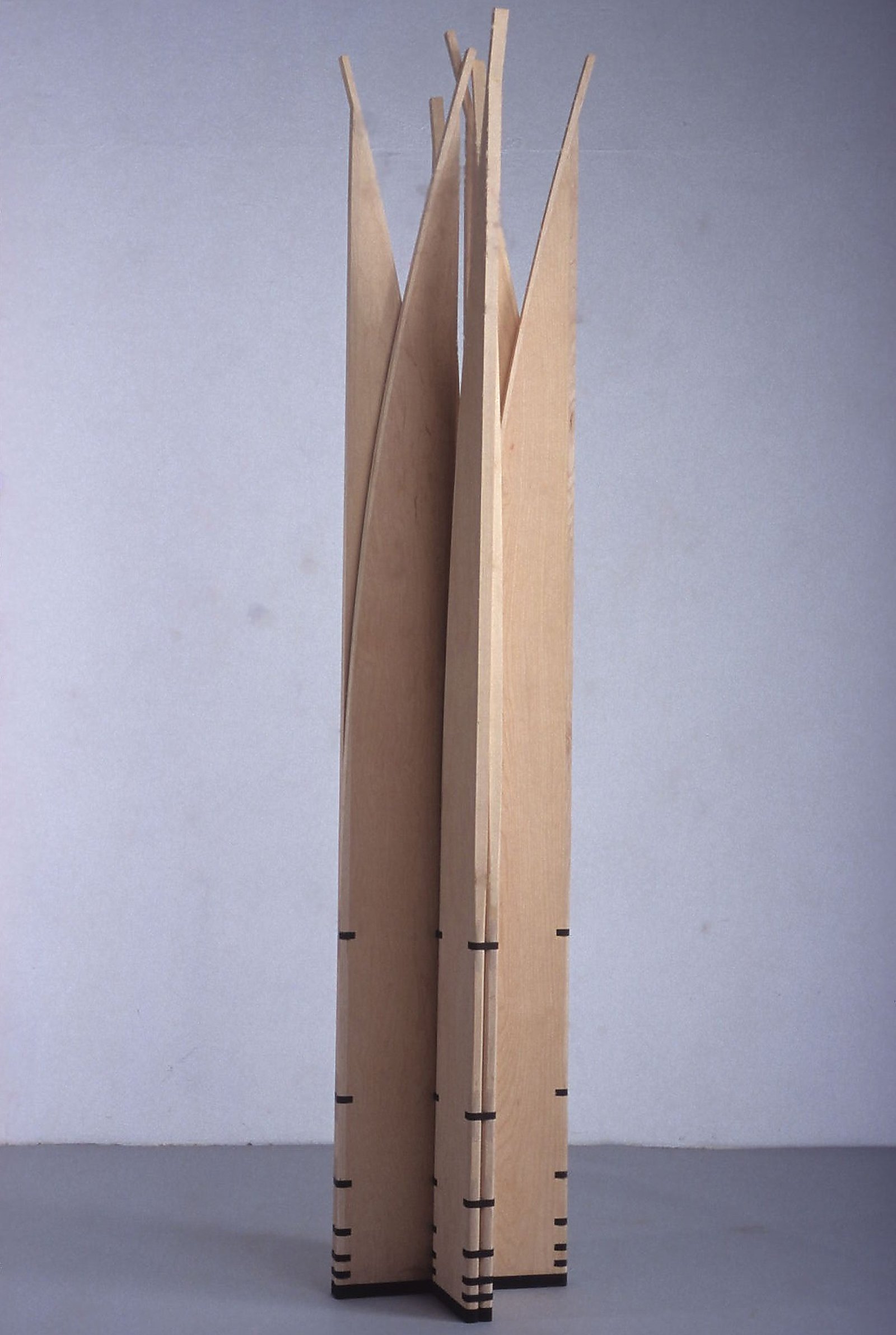 Photograph of the mobile sculpture Velas standing in a star arrangement with slender tapered vertical blades against light grey.