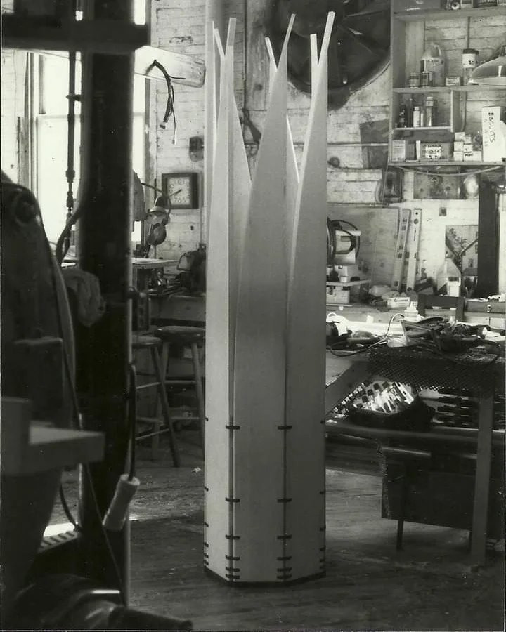 The mobile sculpture Velas stands closed in a cylinder form on a workshop floor.